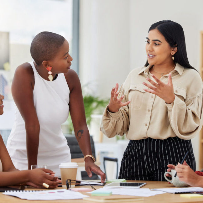 A group of four diverse women having a conversation in an office environment